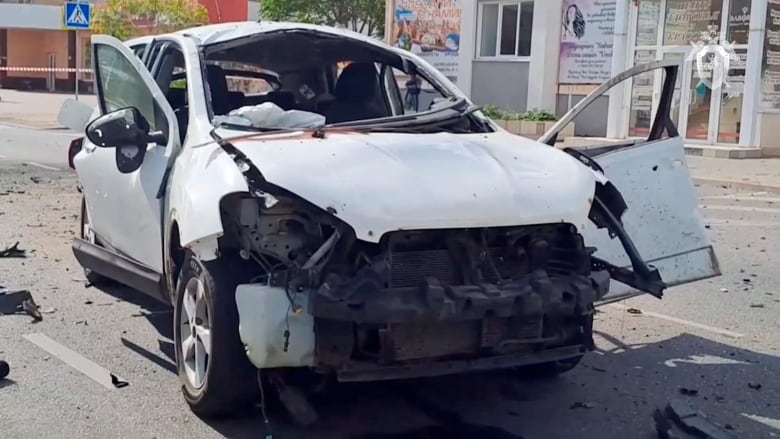 A heavily damaged light-colored car is shown in closeup.