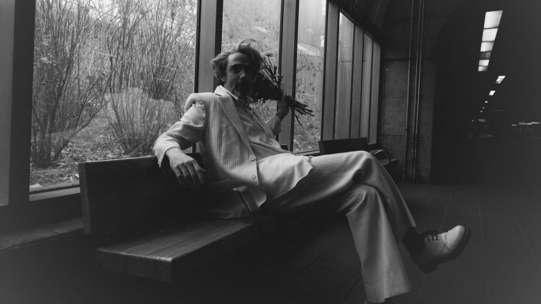 Black and white portrait of Patrick Watson sitting in a metro station, holding a bouquet of flowers.