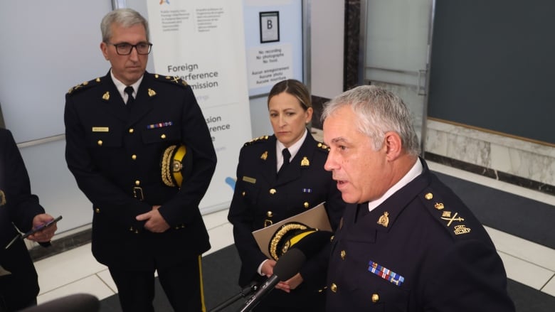 Three uniformed RCMP officers speak with reporters.