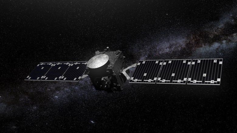 A square spacecraft with long, dark blue solar arrays is seen in space with stars.