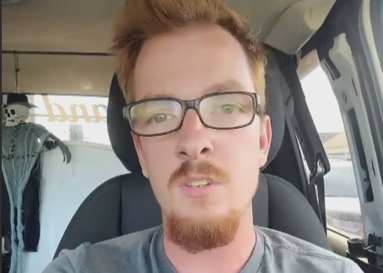 Man with red hair, mustache and beard, sitting in a car.