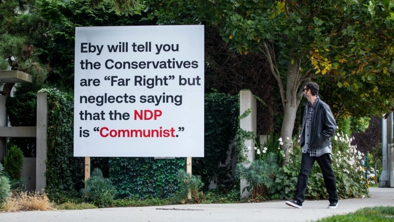 A man walks by a sign that says, 'Eby will tell you the Conservatives are far right but neglects saying that the NDP is communist.' 