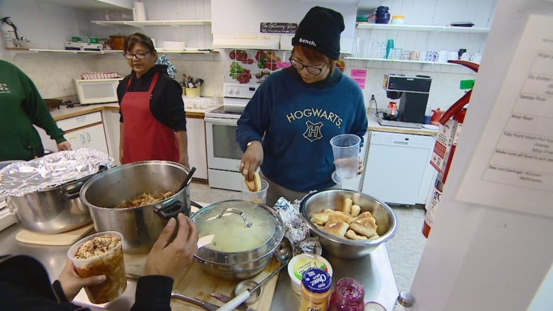 A woman in a Hogwarts sweater and a toque grabs bannock