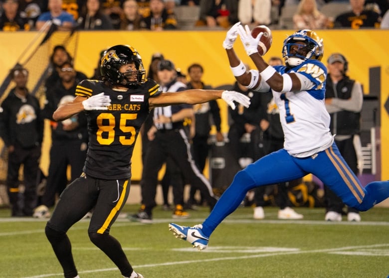 A player in white catches a football in front of a player in black.