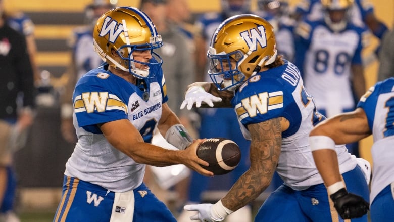 A quarterback in white and blue hands off to a teammate.