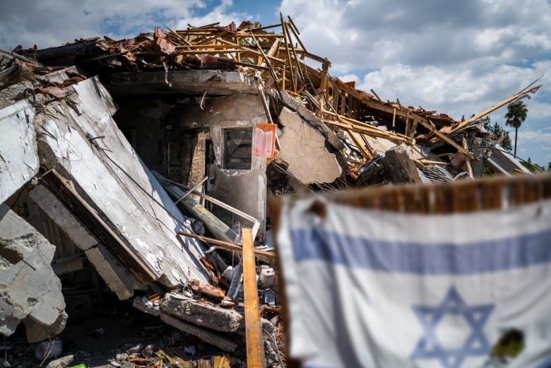 A destroyed building is seen in the background as a flag is seen in the foreground.