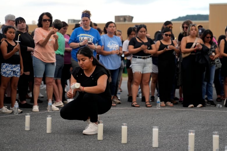 A woman kneels to light a candle as other people stand behind her holding candles.