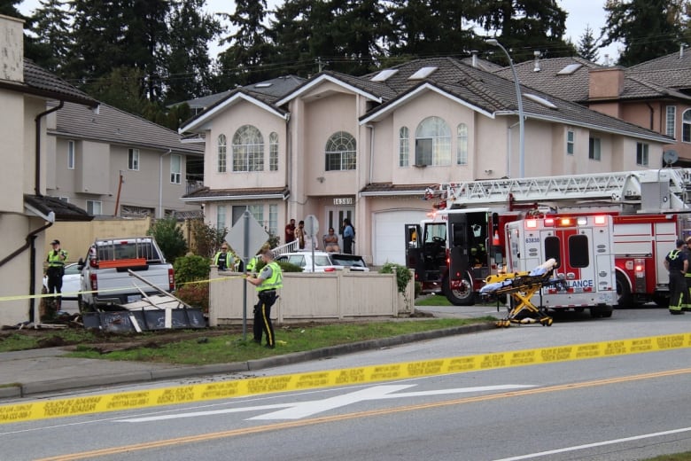 A fire truck and ambulance are seen in the background as a white pickup truck lies behind crime tape and a broken fence.