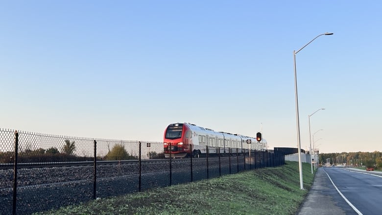 A red public transit train on a rural track on an autumn morning.