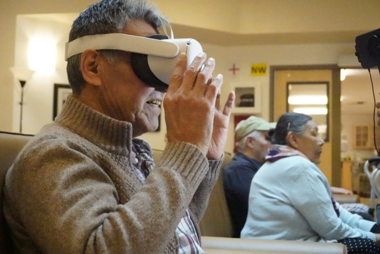 Man sits on coach wearing virtual reality headset.