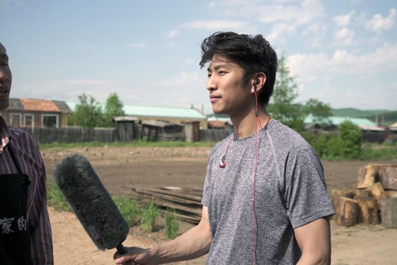  An Asian man hold a microphone while interviewing another person 