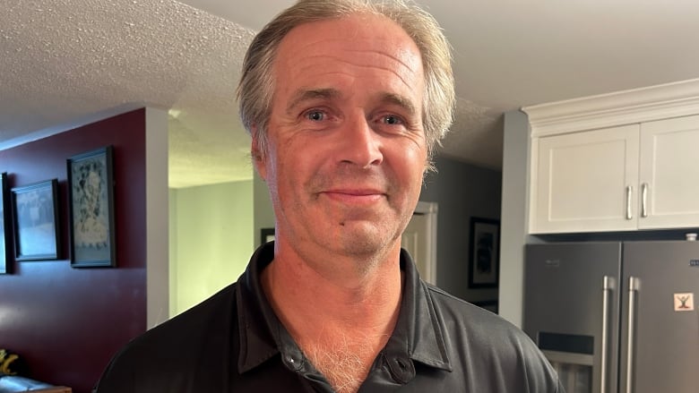 Man in a black golf shirt stands in a kitchen.