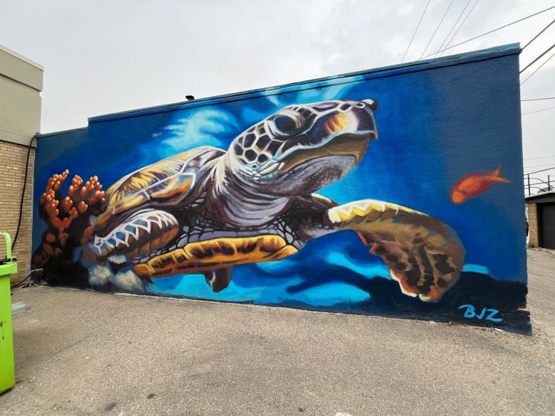 A mural of a brightly coloured turtle floating its way through water. 