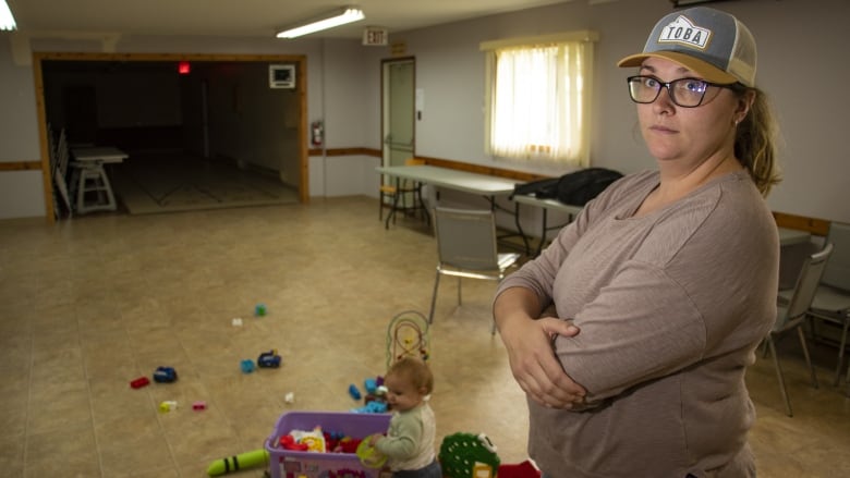 A woman stands with a baby in the background.