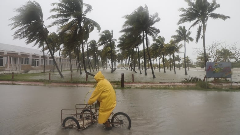 A person in a raincoat rides a bike through a flooded street.