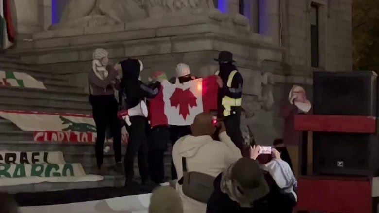 Masked protesters burn an upside-down Canadian flag.