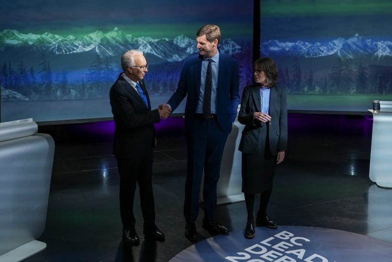 Two men shake hands as a woman looks on.