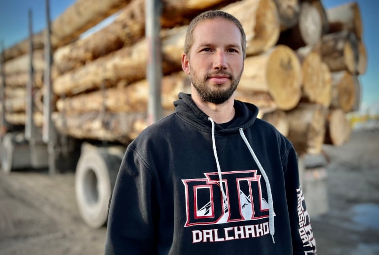 A man with a beard in front of a logging truck. 