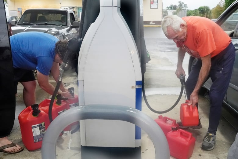 Two men are shown on opposite sides of gas station pumps, filling up red cannisters.