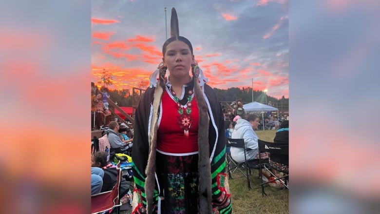 A person is seen standing outside wearing traditional powwow regalia.