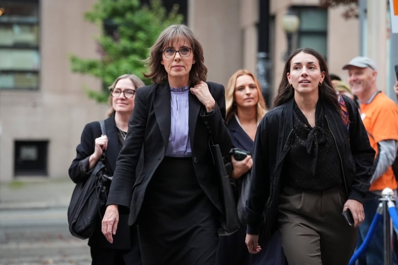 A group of women, led by the Green Party leader wearing a blue coat over a light blue top, walk toward the camera.