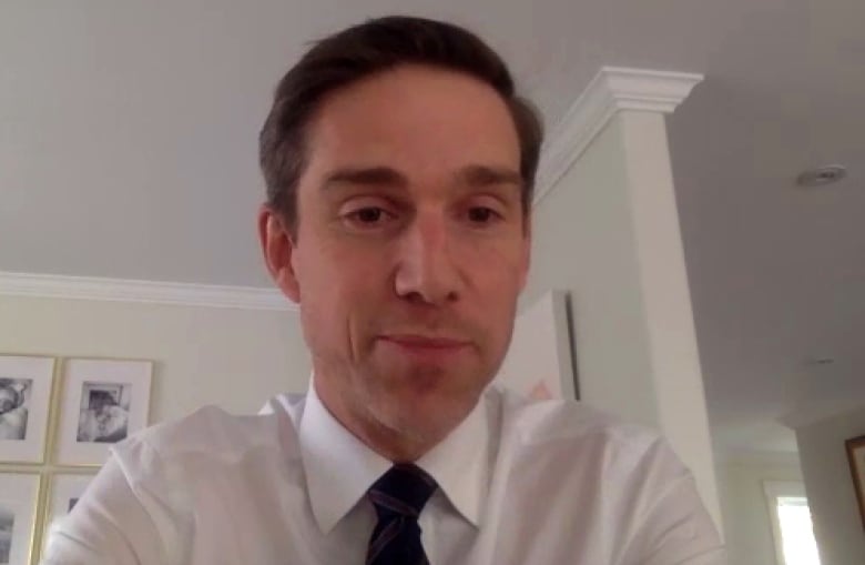 A man wearing a white shirt and tie sits in a living room while on a video call.