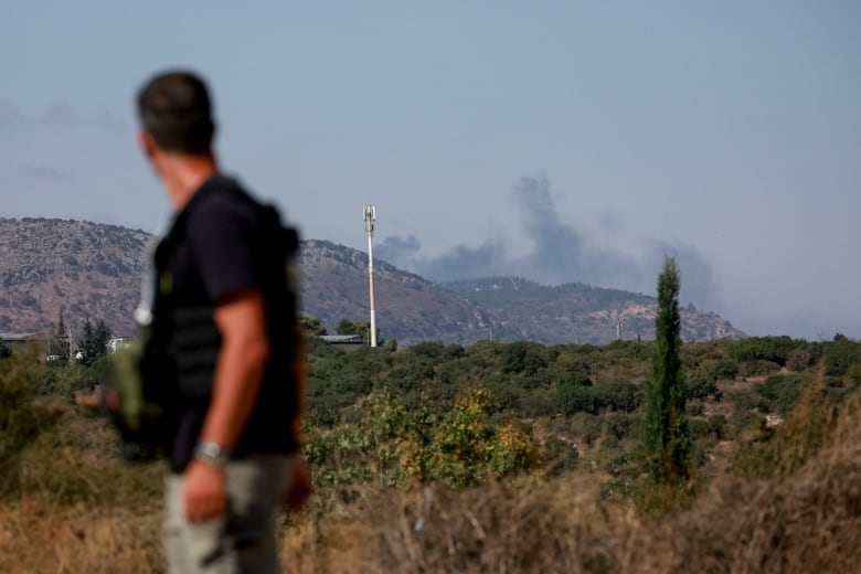 A man stands facing hills with smoke