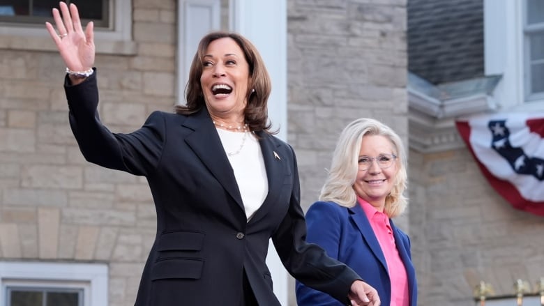 Harris waves while walking with a smiling Cheney on a stage