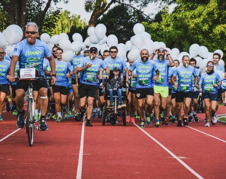 A group of people run on a track, carrying white balloons, and wearing in matching sky-blue shirts that read 