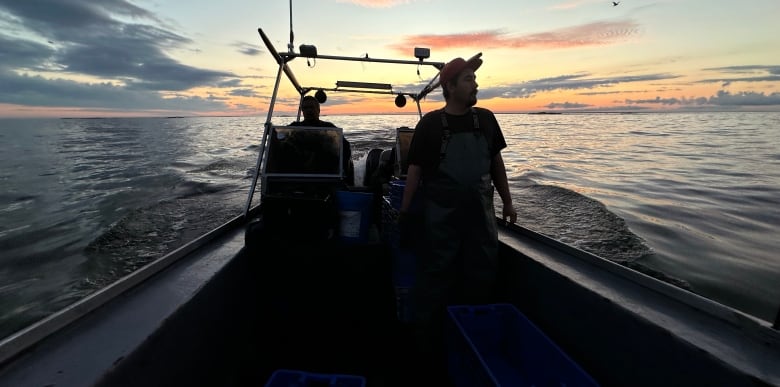 Commercial fishers on a commercial fishing boat are pictured in partial silhouette while out on a large lake.