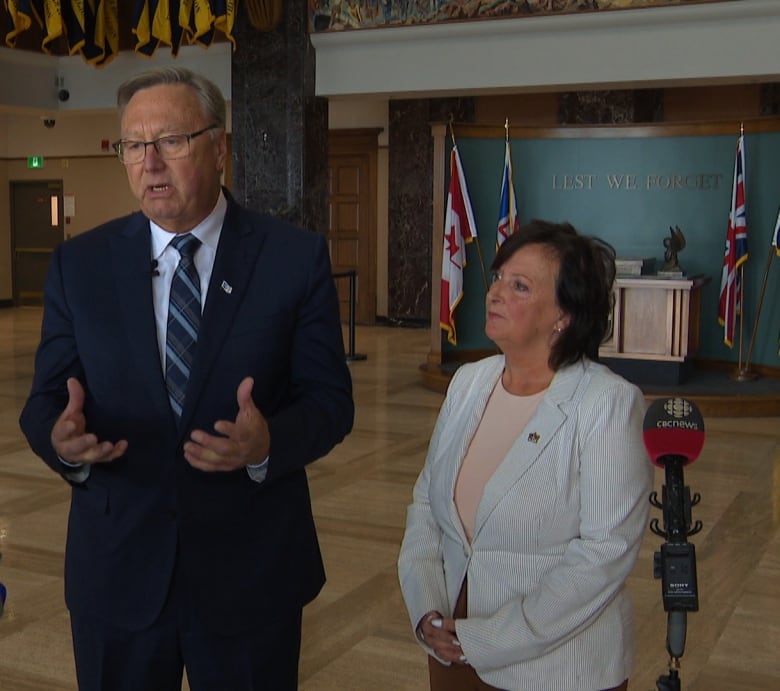 A tall man and short woman wearing suits stand in the lobby of Confederation Building.