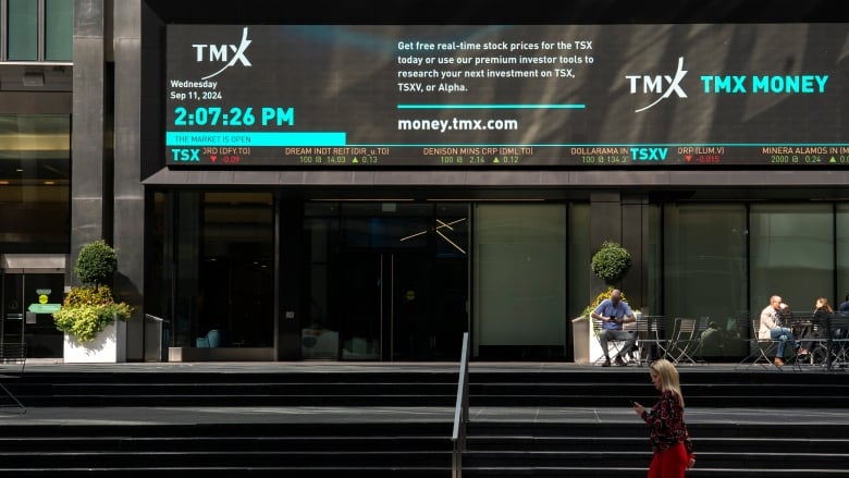 A woman walks by a building with a stock exchange sign.