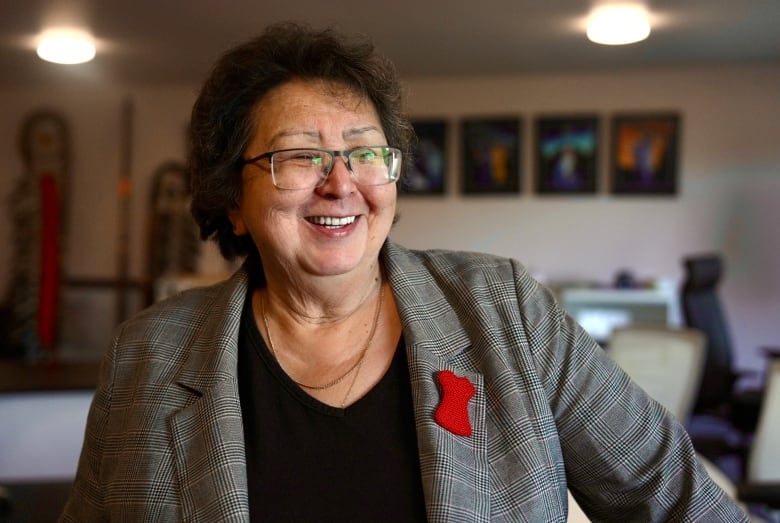 A woman wearing a black shirt and grey blazer with a red dress pin is pictured in a band office council chambers.