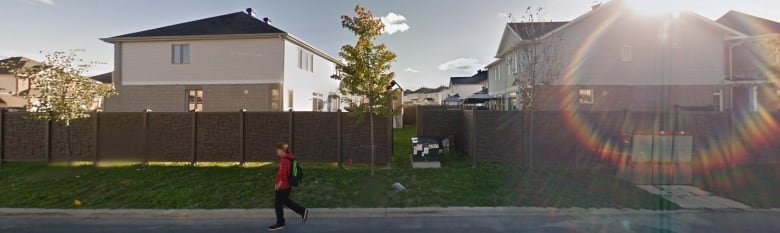 A boy walks by a brown fence.