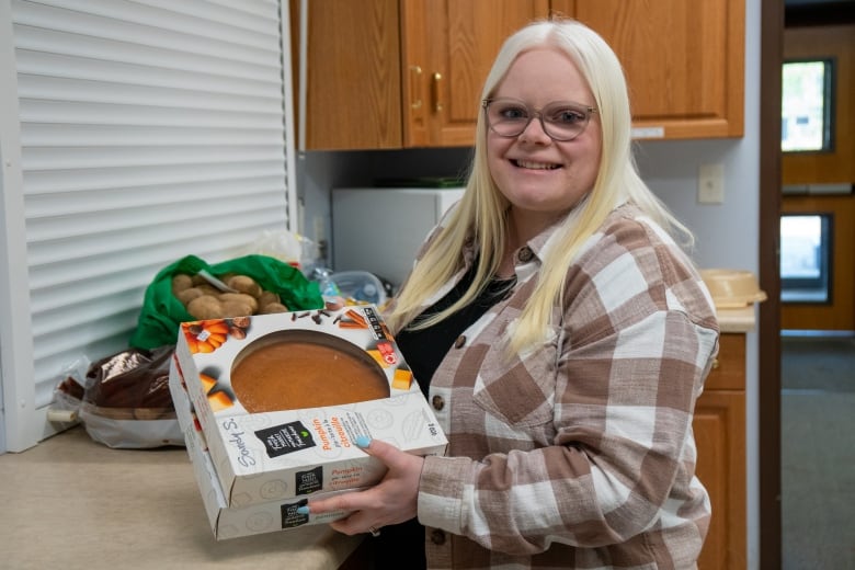 A person stands in a kitchen holding boxes of pie. They are smiling.