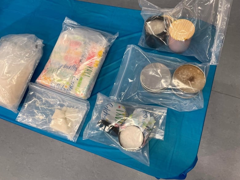 A handful of items, including candles and soap, are seen inside clear bags on a table covered in a blue cloth. 