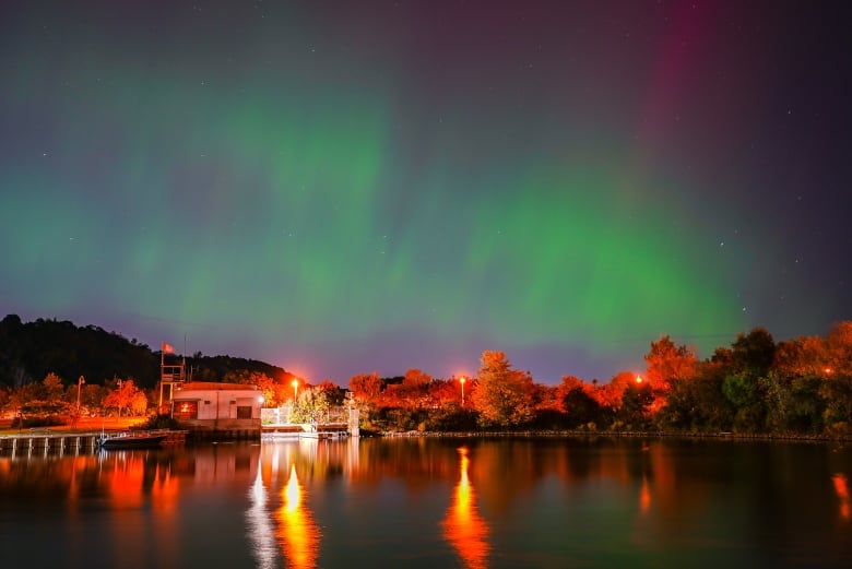 The northern lights shine above a lake and cottage in Scarborough, streaking the evening sky with bright greens