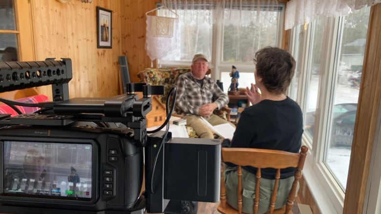 Two people sitting across from each other, with a camera filming them