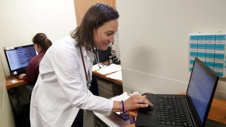 A doctor leans over to type on a laptop.