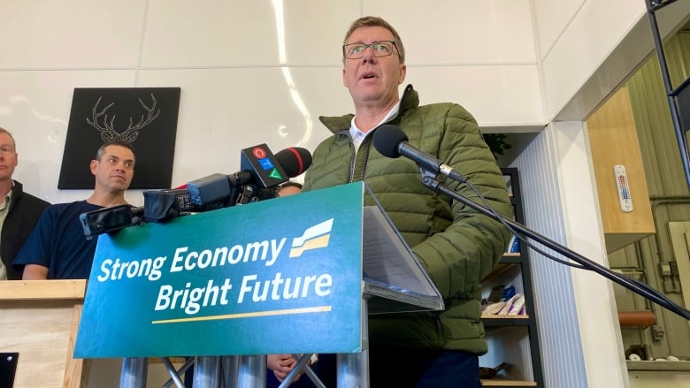 A man in a green jacket stands at a podium.