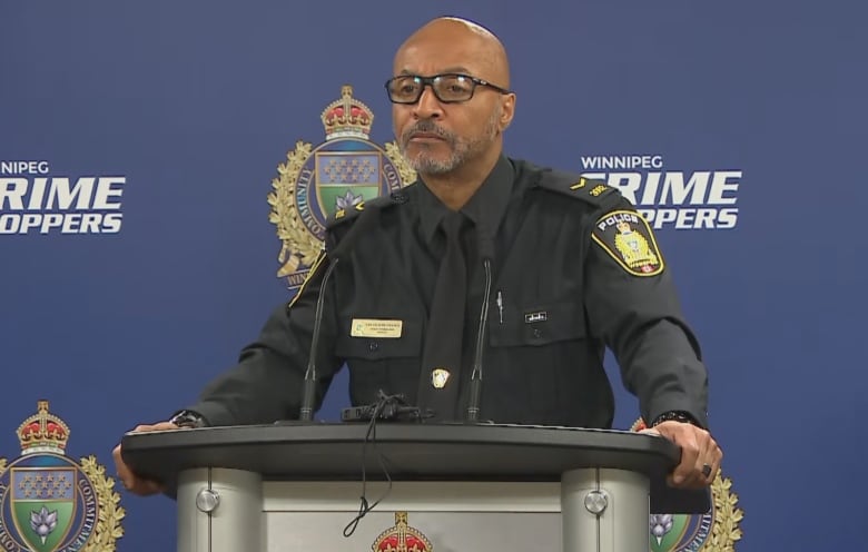 A police officer stands at a podium with microphones