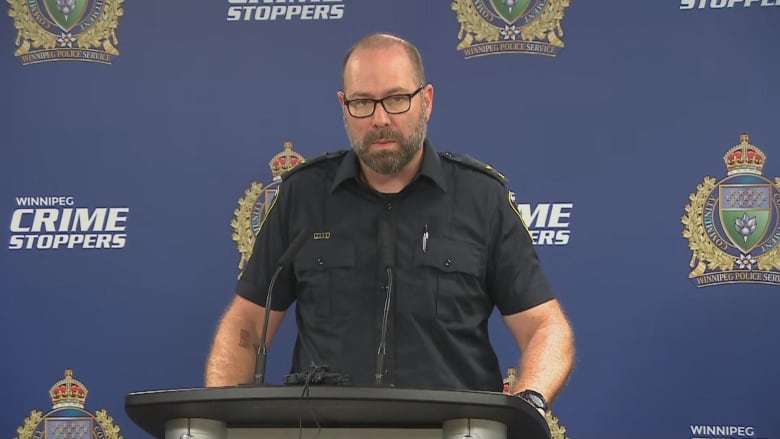 A man in a police uniform speaks at podium.