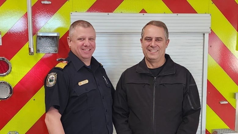 Two men standing infront  of a fire truck