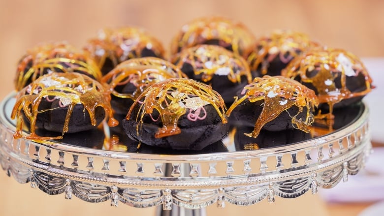 A silver cake stand with 10 round, fat dark chocolate cookies on it. Each cookie has a candied caramel cage on top.