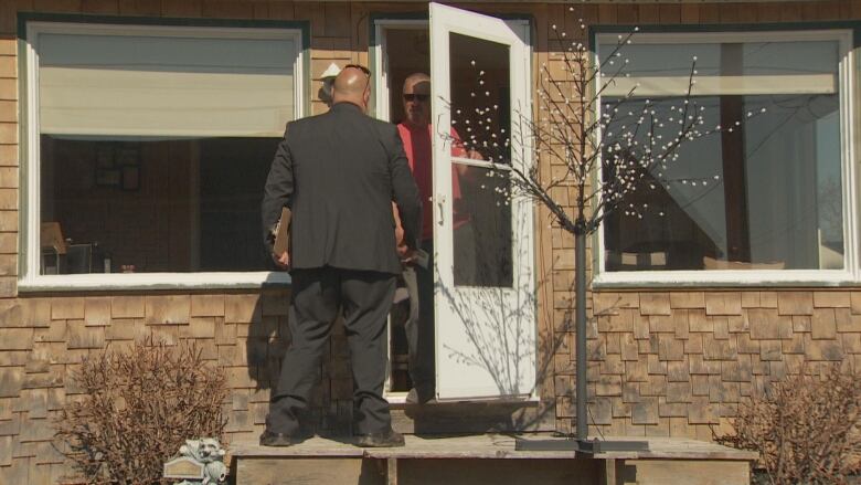 A man standing on someone's door stoop and talking to a man who is inside.