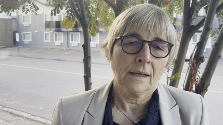 A woman with glasses stands outside.