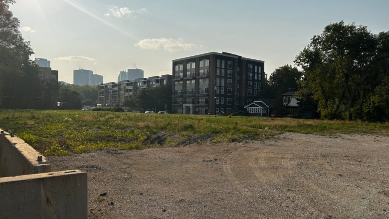 Tire tracks are seen in an empty lot, with a four-storey apartment building in the background.