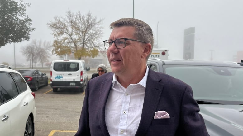 A man in a suit stands outside in a parking lot.