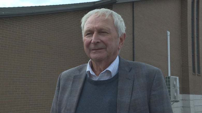 A man is pictured looking at the camera in front of a brick building.