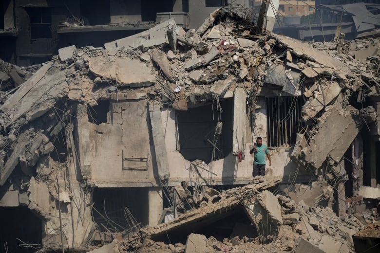 A person stand amid the rubble of a destroyed building.